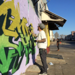 Adam Stab paints a mural on a wall on the street.