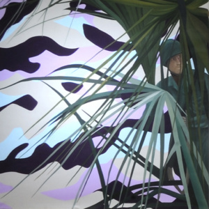 A soldier wearing camouflage peeks around heavy vegetation. 