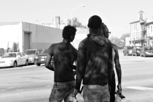 Three young African American men hold spray bottles and rags as they stand on a street corner. 