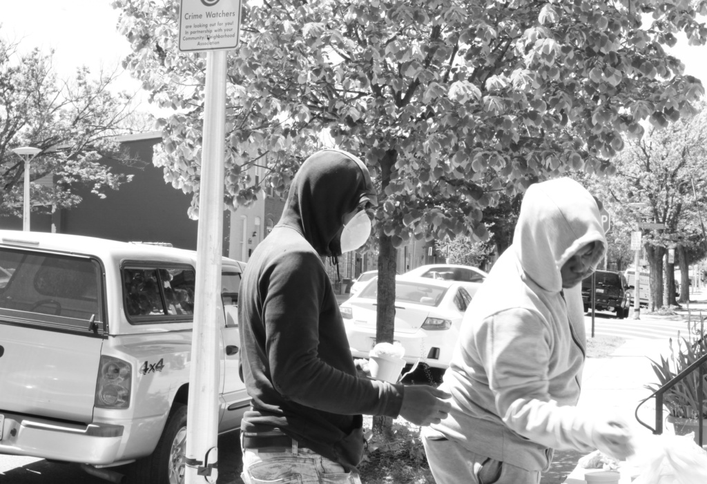 Two people wearing face masks and sweatshirts stop to pick up food. 