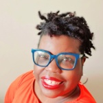 Daisy Brown wears blue, square eye glasses and bright red lipstick.