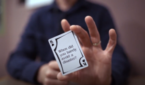 A person with a blue shirt holds a card close to the camera that has a question on the face of the card.