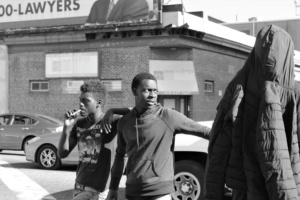 A group of young men talk and smoke near a busy intersection in Baltimore.