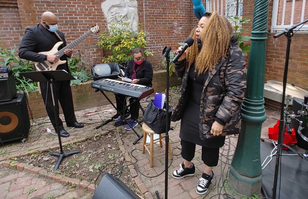 A group of three musicians perform a concert in the bricked garden of the Peale.
