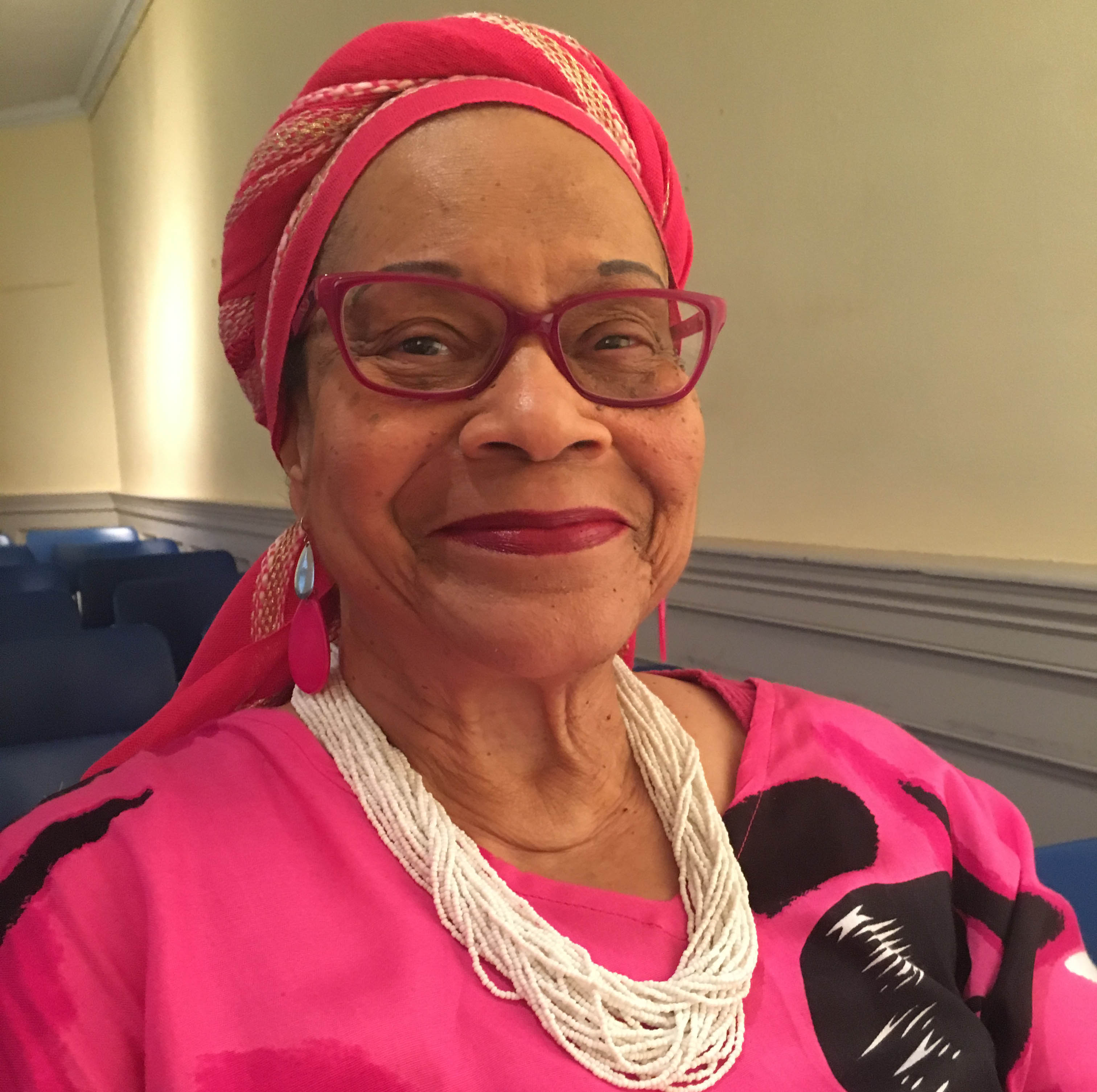A woman in a bright pink shirt and white necklace.