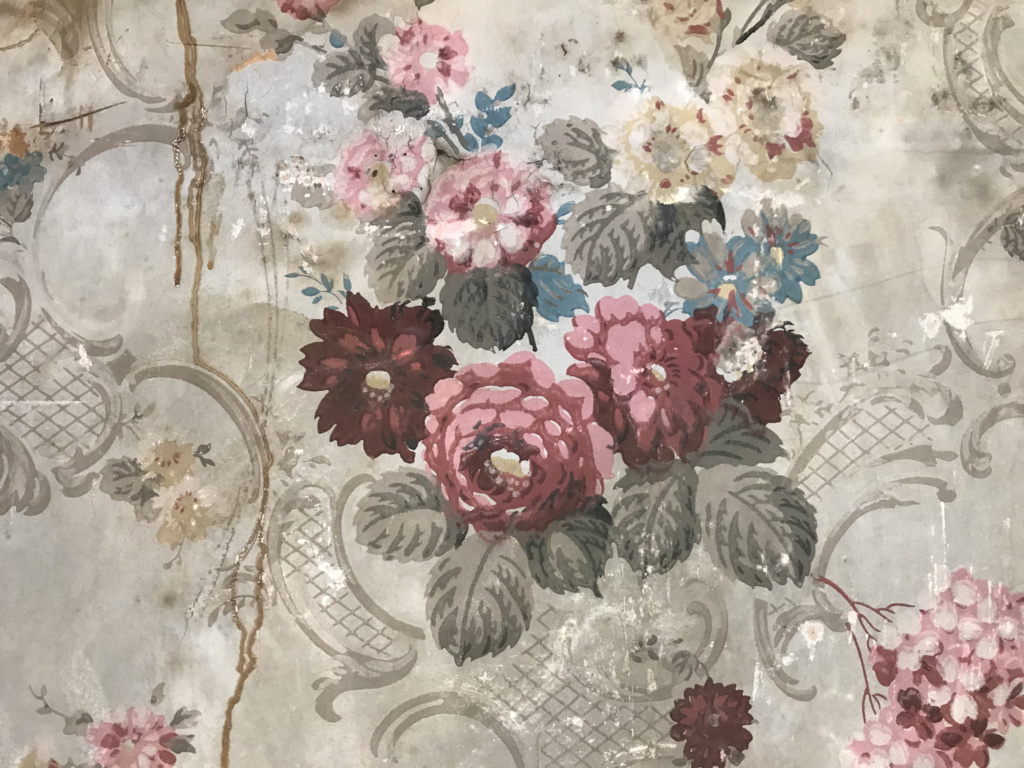 Historic wallpaper showing red and pink flowers and a cross-hatched basket pattern behind it. 