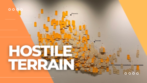On the left, an orange triangle with the words, Hostile Terrain, in white, bold font. In the center, a photo of tags hanging on a map, and on the right, a yellow triangle.
