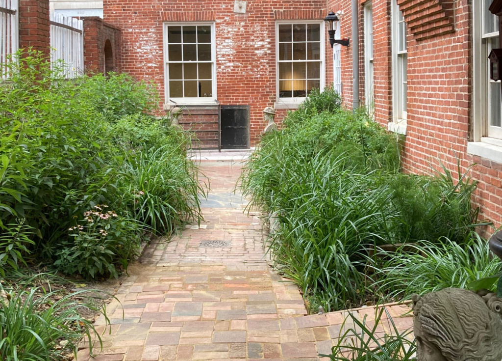A brick walkway leading to a garden with a brick building in the background.